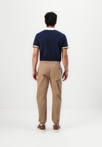 Marinblå kortermet polo med hvite og beige detaljer, kombinert med lysebrune elastiske cargo bukser og brune sneakers.