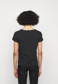 Černé tričko s krátkými rukávy a kulatým výstřihem, zobrazené ze zadní strany, vyrobené z měkké bavlny, s rovním lemem a minimalistickým designem.