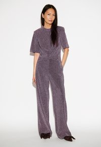 Paarse, sprankelende jumpsuit met korte mouwen, een losse pasvorm en een hoge taille. Heeft wijde benen en een zachte, gestructureerde afwerking.