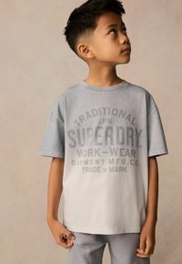 Heledate halli puuvillane T-särk lühikeste varrukatega, mille esiküljel on tumehall tekst "Superdry Work-Wear." Mudel kannab sobivaid halli pükse.