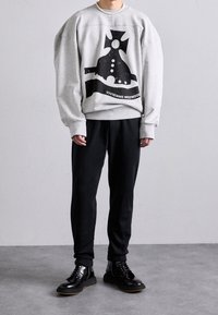 Grå sweatshirt med stor svart grafik och text, tillsammans med svarta sweatpants och blanka svarta snörkängor. Enkel, avslappnad design.