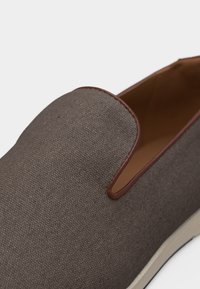 Καφέ παπούτσι τύπου slip-on με υφή, με δερμάτινη επένδυση γύρω από το άνοιγμα και ανοιχτόχρωμη σόλα, σε κοντινή λήψη.