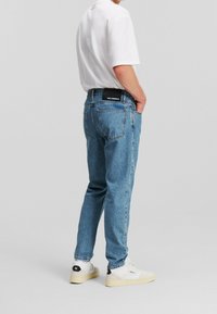 Jeans de mezclilla azul claro con un corte relajado, que cuentan con un parche trasero con logotipo, cinco bolsillos y una textura ligeramente desgastada.