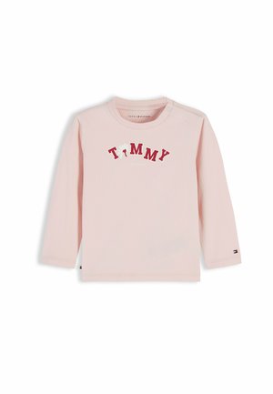 Jasnoróżowa bluzka z długim rękawem dla malucha z napisem "TOMMY" czerwonymi literami na piersi oraz małym logo Tommy Hilfiger na mankiecie rękawa.