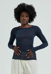 Long-sleeve top in dark navy, made of soft, stretchy material. Features a rounded neckline and fitted shape, paired with loose cream trousers.