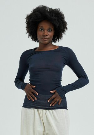 Long-sleeve top in dark navy, made of soft, stretchy material. Features a rounded neckline and fitted shape, paired with loose cream trousers.