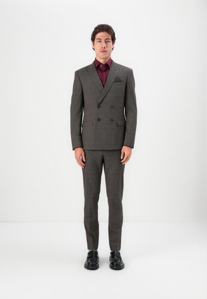 Costume double poitrine à carreaux gris, avec une chemise bordeaux contrastante, un mouchoir de poche noir et des chaussures noires brillantes. Coupe ajustée.