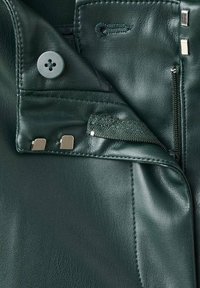 Donker groene leren jas detail met een knop, metalen accenten en een ritssluiting pocket met een geweven stofvoering.