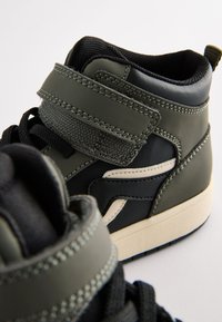 Baskets montantes en cuir synthétique combinant vert foncé et noir. Elles comportent une bride à scratch et des accents blancs contrastants.