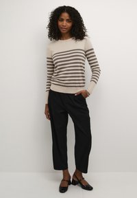 Maglione a righe beige e marrone con maniche lunghe, abbinato a pantaloni neri a gamba larga e scarpe slingback nere. Texture a maglia liscia.
