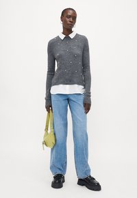 Grå strikkegenser med perlepynt, hvit skjorte med krage under, lyseblå jeans og en liten grønn håndveske. Sorte platåsko.