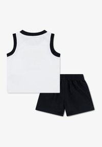 Valge varrukateta top musta äärisega, ühendatud mustade lühikestega; materjal tundub kerge ja hingav, sobib aktiivseks kandmiseks.