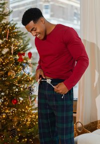 Rode blouse met lange mouwen en een ronde hals, gecombineerd met geruite pyjamabroek in donkergroen en marineblauw, met een taillekoord en zijzakken.