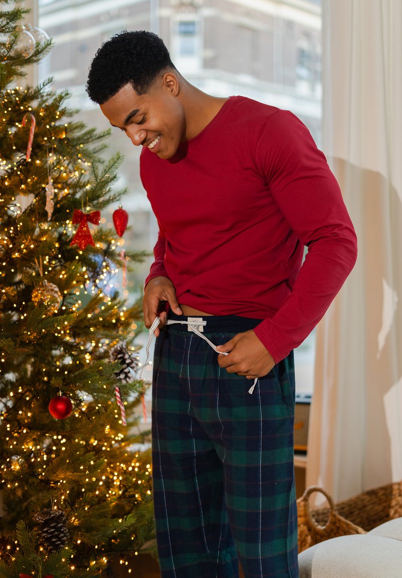 Rode blouse met lange mouwen en een ronde hals, gecombineerd met geruite pyjamabroek in donkergroen en marineblauw, met een taillekoord en zijzakken.