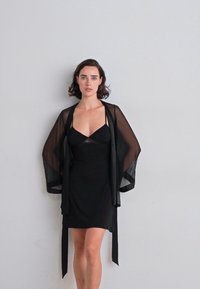 Crni prozirni kimono s otvorenim rukavima preko prilagođene crne slip haljine, s glatkom teksturom i jednostavnim dizajnom bez uzoraka.