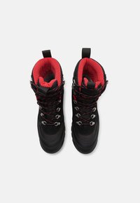 Black hiking boots with red mesh lining, featuring metal eyelets, black laces, and rubber soles for traction.