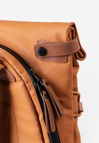 Zaino in pelle marrone chiaro con chiusura a zip, hardware nero, texture liscia, parte superiore arrotolata e una cinghia laterale per una chiusura sicura.