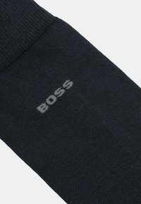 Calzino blu scuro con polsino a coste, realizzato in tessuto morbido. Presenta il logo "BOSS" in grigio chiaro vicino alla caviglia.