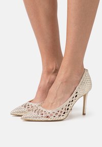 Scarpe con tacco a spillo in maglia metallizzata oro, con punta affusolata e design a rete aperta, caratterizzate da un elegante tacco stiletto per un'altezza aggiuntiva.