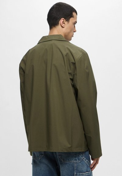 Giacca verde oliva con vestibilità rilassata, caratterizzata da un colletto classico e maniche lunghe. Il tessuto è liscio con texture minimal.