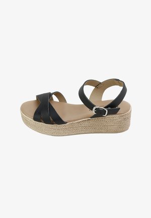 Sandalia de cuña negra con tiras cruzadas, hebilla en el tobillo y plataforma entrelazada.