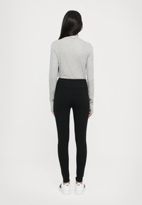 Grijze lange mouwtop in combinatie met zwarte leggingbroeken. De broeken hebben een hoge tailleband en zijn aansluitend bij de enkels. Witte sneakers maken de outfit compleet.