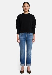 Czarny skrócony sweter z szerokimi rękawami, niebieskie dżinsy proste z podwiniętymi nogawkami i baleriny w leopardzi wzór, na białym tle.