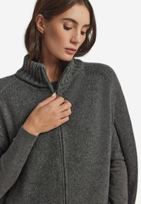 Gråstickad zip-up tröja med hög krage, med ett texturerat ribbat mönster och en avslappnad passform. Mjuk, varm tyg.