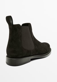 Stivale Chelsea in suede nero con pannelli elasticizzati sui lati, punta rotonda e suola piatta in gomma, dotato di un linguetta sul tallone per facilitare l'inserimento.
