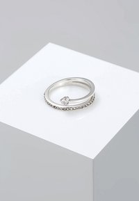 Zilveren ring met een gladde band en een cluster van kleine heldere stenen langs de band, met een enkele grotere heldere steen die onder een hoek is gezet.