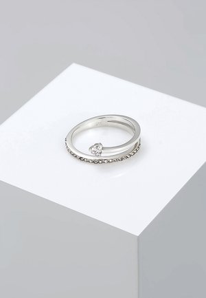 Silberring mit einem glatten Band und einem Cluster aus kleinen klaren Steinen, die das Band schmücken, mit einem einzelnen größeren klaren Stein, der schräg eingesetzt ist.
