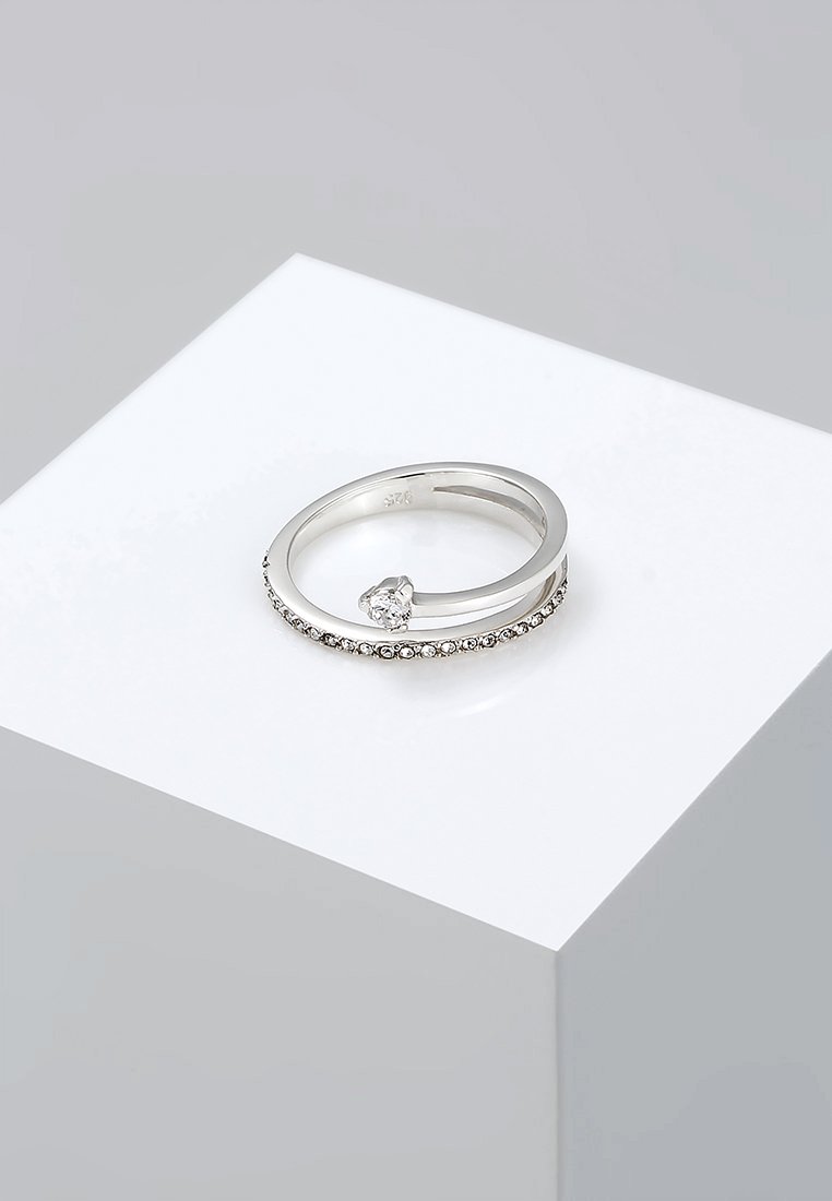 Zilveren ring met een gladde band en een cluster van kleine heldere stenen langs de band, met een enkele grotere heldere steen die onder een hoek is gezet.