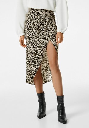 Midi-Rock mit Leopardenmuster aus leichtem Stoff, mit hohem Schlitz auf einer Seite, kombiniert mit schwarzen Stiefeletten für Kontrast.