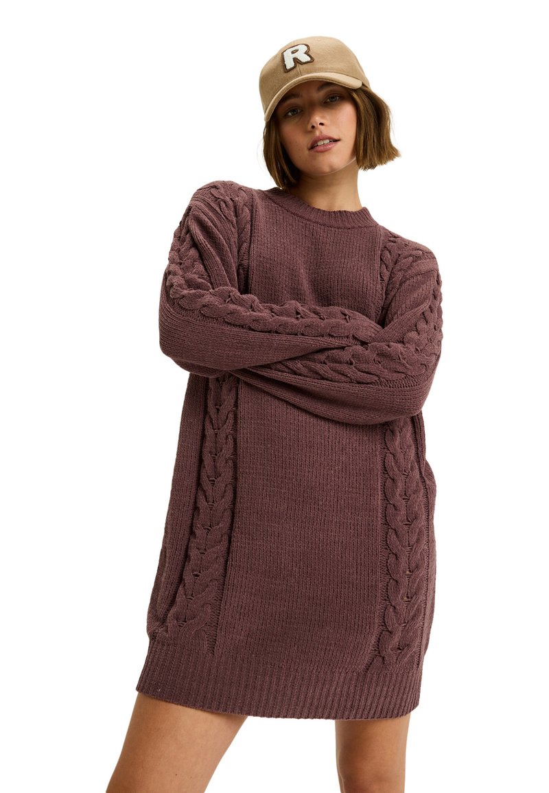 Sweter-dres w kolorze burgundowym z akcentami warkocza na rękawach. Posiada okrągły dekolt i luźny krój.