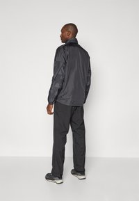 Schwarze leichte Jacke mit hohem Kragen und langen Ärmeln, kombiniert mit dunklen Hosen und Sneakers, mit einer glatten, eleganten Textur.