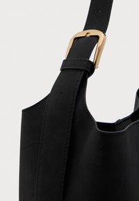 Sort lædertaske-strop med guld-tone spænde mod en ensfarvet hvid baggrund.