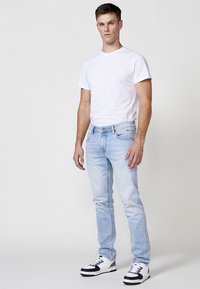 Jeans de mezclilla azul claro y una camiseta blanca ajustada. Los jeans tienen una textura ligeramente desgastada, con un diseño estándar de cinco bolsillos y trabillas para el cinturón.