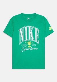 Groene katoenen t-shirt met grote witte "NIKE" tekst, een trofee graphic, en "EST. 1972 Sportswear" in witte en gele accenten. Korte mouwen.