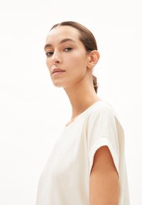 T-shirt court à manches courtes couleur beige clair avec une coupe décontractée. Il présente un col rond, une texture douce et de subtils détails à l'avant.