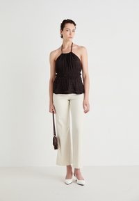 Crna halter bluzica s teksturiranim materijalom, uskim strukom i peplum dizajnom, u kombinaciji s kremasto bijelim širokim hlačama i bijelim cipelama s oštrim vrhom.