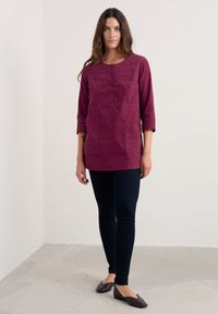 Bordo tunika ar trīs ceturtdaļu piedurknēm, teksturēta auduma, ar pogu auklu; kopā ar tumši ziliem zīmuļbiksēm un plakanām kurpēm.