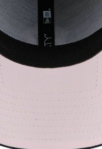 Mütze aus leichtem pinkem Stoff, mit schwarzem Saum am Rand und einem strukturierten Innenfutter. Enthält ein Markenschild innen mit Logo-Details.