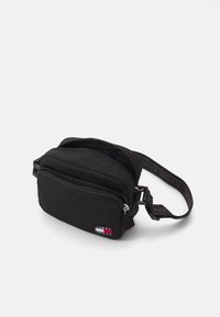 Borsa a tracolla nera in tessuto con due scomparti con zip e una tracolla con il marchio "TOMMY JEANS." Forma rettangolare e superficie liscia.