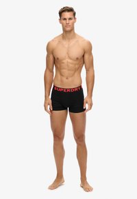Boxer-briefs noirs avec un logo "SUPERDRY" rouge sur la ceinture. Design lisse et ajusté avec une texture douce, idéal pour un usage quotidien.