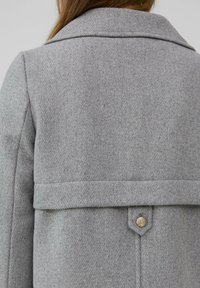 Manteau en mélange de laine gris avec un col structuré, un détail de couture horizontal et un accent de bouton doré au dos. Fini en tissu texturé.
