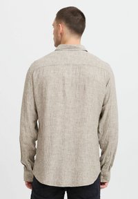 Lysbrun skjorte med knapper, der har en subtil stribet tekstur, lange ærmer og en buet kant. Kraven er standard med knapdetaljer.