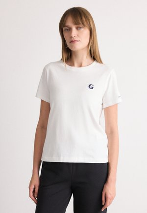 T-shirt bianco in cotone con maniche corte, collo rotondo e un piccolo logo blu "G" sul petto. Indossato con pantaloni scuri.