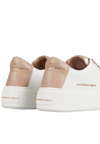 Sneaker in pelle bianca con dettagli beige, retro testurizzato e branding in rilievo. Suola bianca spessa con dettagli di design minimi.