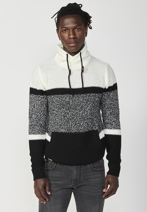 Suéter de punto con cuello cisne, con un patrón a rayas en negro, blanco y gris. Tejido texturizado con un bolsillo frontal y cordones.