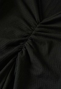 Černá texturovaná látka s mačkaným vzorem, která obsahuje nařasené části, jež vytvářejí objem a hloubku po celé ploše materiálu.